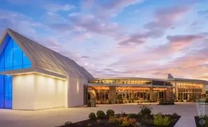 Modern building with a large blue triangular window, lit up at dusk under a colorful sky.