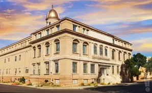 A tan, three-story building with arched windows and a golden dome under a dramatic sky.