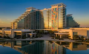 A modern hotel with a large colorful mosaic on the facade, reflecting in a calm pool of water.