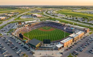 Aerial view of a baseball stadium with a packed crowd, surrounded by parking lots and suburban development.