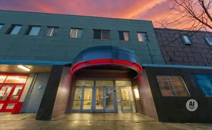 A building entrance with red neon lights, glass doors, and a pink sky.
