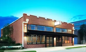 Brick building with large windows and a black awning, under a bright blue sky.