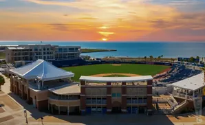 Baseball stadium by the ocean at sunset, with a panoramic view of the field, stands, and buildings.