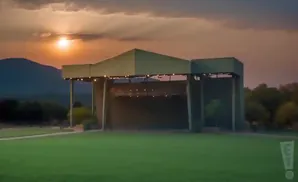 Outdoor amphitheater stage with a grassy lawn in the foreground, mountains and sunset in the background.