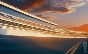 A race track in front of stadium seating under a colorful sunset sky.