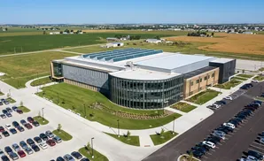Aerial view of a modern building with a curved glass facade and a large parking lot filled with cars.