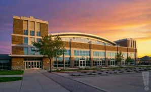 Modern brick building with large windows and a curved glass roof at sunset.