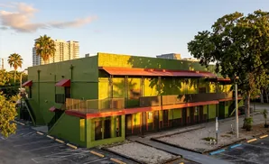 Bright green building with red awnings and balconies, parked cars, and trees.