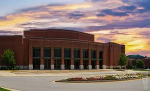 A brick building with large windows and a curved facade, set against a dramatic sunset sky.