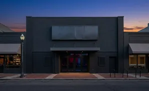 Dark building with large sign above entrance. Bar visible to the left, office to the right. Street lamp in foreground.