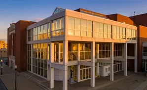 A modern building with large glass windows reflecting the sunset, juxtaposed with an older brick structure.