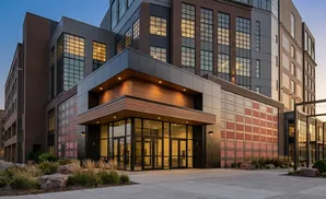 Modern apartment building entrance with large glass doors and windows, accented with wood and brick.