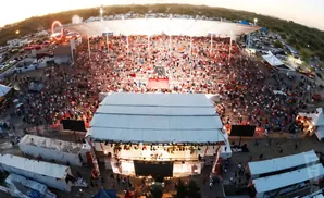 An aerial view of a crowded outdoor concert with a stage and seating area.