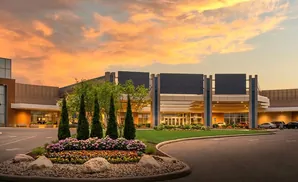 A modern building entrance with a colorful flower bed and dramatic sunset sky.