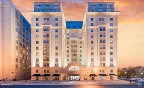 A grand, illuminated hotel with two towers stands tall against a dramatic sunset sky.