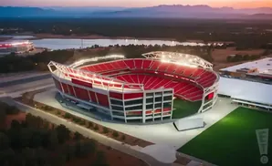 Aerial view of a large, red-seated stadium at dusk, with distant mountains and a lake.