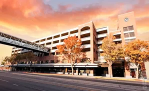 A multi-story brick building with a skybridge and autumn trees against a colorful sunset sky.