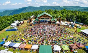 Aerial view of an outdoor music festival with a large crowd gathered in front of a stage, surrounded by tents and campers.
