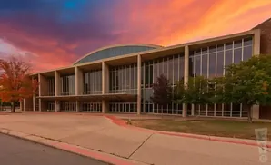 Modern building with large windows and a curved glass roof under a vibrant sunset sky.