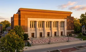 An imposing brick building with neoclassical columns and a patterned plaza in front.