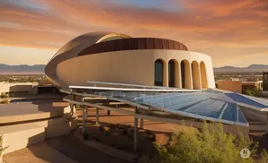 Desert sunset illuminates a futuristic curved building with arched windows and a glass-covered walkway.