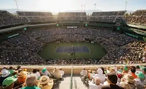 An aerial view of a tennis match in a packed stadium, with spectators in the foreground.