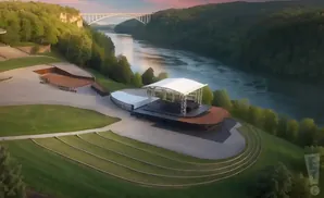 Outdoor amphitheater stage by a river with a bridge in the distance.