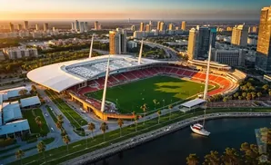 Aerial view of a stadium at sunset, with a city skyline in the background and a boat in the foreground.
