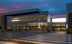 A modern convention center at dusk with a bright marquee and cars parked outside.