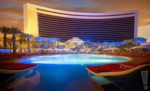 A luxury resort pool at dusk, with palm trees, lounge chairs, and a curved hotel in the background.