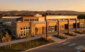 Modern brick building with large windows and a covered walkway, bathed in golden sunset light with distant mountains.