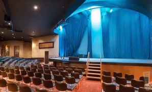 An empty theater with blue curtains on stage and rows of seats.