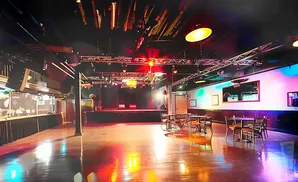 A nightclub stage, tables, and bar area lit with colorful stage lights.