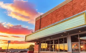 A storefront with a blank marquee under a colorful sunset sky.