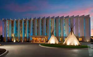 Hotel lit with blue lights at dusk, with two teepees in front.