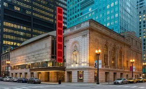 Theater with modern and historic architecture, neon sign, and taxis on a city street at dusk.