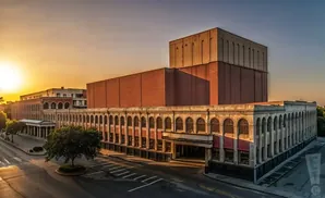Sunset over an old brick building with a long arched facade and a large concrete structure on top.