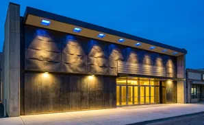Modern building entrance at dusk with illuminated facade and blue uplighting.