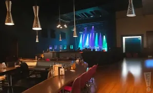 A dimly lit concert venue with a stage set up for a band, and a bar area in the foreground.