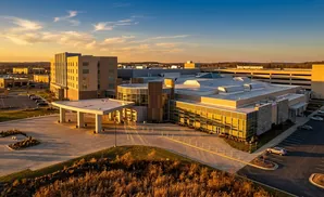 An aerial view of a modern hospital and parking garage at sunset.