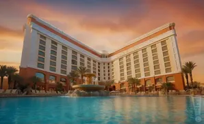 A large, U-shaped hotel with an orange and white facade, featuring numerous windows, stands beside a vibrant blue swimming pool.