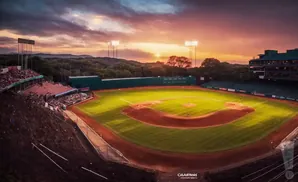 Baseball field at sunset with dramatic sky and stadium lights on.