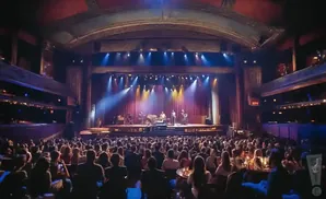 A band performs on a brightly lit stage in a crowded, ornate theater.