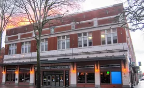 Red brick building with large windows and a dark awning over the storefronts.