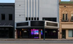 A modern building with a marquee and colorful interior glows next to historic brick buildings.