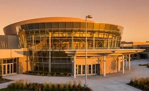 Modern glass-fronted building with curved architecture illuminated by sunset.