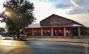 A rustic restaurant with a metal roof and stone accents sits under a cloudy sky.