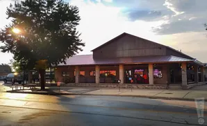 A rustic building with a metal roof and stone accents, featuring a covered patio area and neon signs.