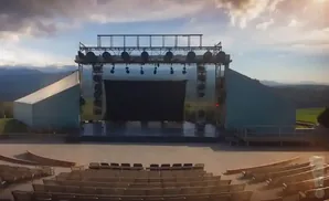 Outdoor amphitheater with stage and seating in front of a mountain landscape.