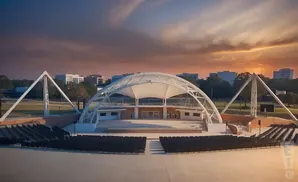 An outdoor amphitheater with a white arched canopy stage and tiered seating at sunset.